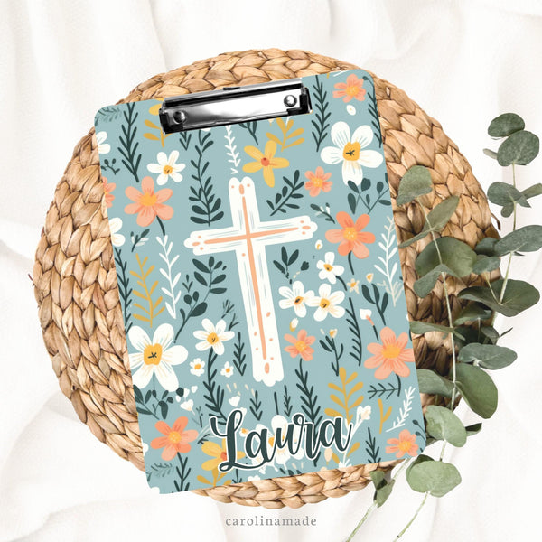This beautiful double sided clipboard features a muted blue background with flowers in coral, white and yellow. There is a big cross in the center of the clipboard and it is personalized at the bottom with a name.