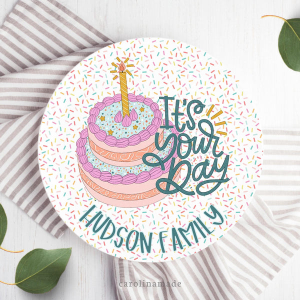 This fun 10 inch celebration plate features a rainbow sprinkle background with a big cake in the center. Text says Its your day and the bottom is personalized with the family name.