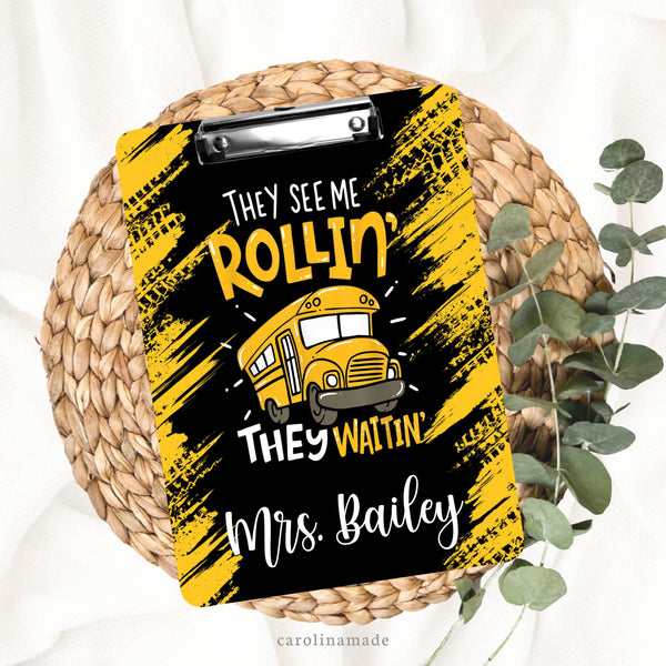 This double sided clipboard features a black background with distressed yellow tire tracks. The center has a bus and says They see me rollin, they waitin. It is personalized at the bottom with a bus drivers name.