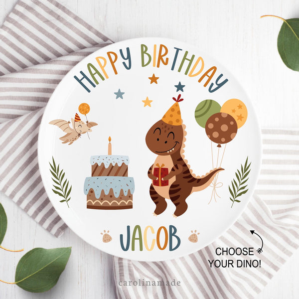 This white Happy Birthday plate features a fun colorful design with dinosaur, presents, cake, balloons, stars, dino feet and leaves. The top says happy birthday and the bottom is personalized with childs name.