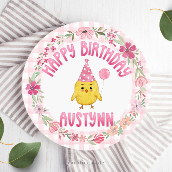 This ten inch birthday plate features a pink gingham ring with a floral wreath and pink text that says Happy Birthday and is personalized with your childs name. The center is a baby chick wearing a birthday hat & balloon.