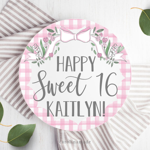 This white 10 inch plate features a pink bow with flowers and greener at the top and a gingham scallop edge around the edge. The center says Happy Sweet 16 and is personalized with your daughters name.