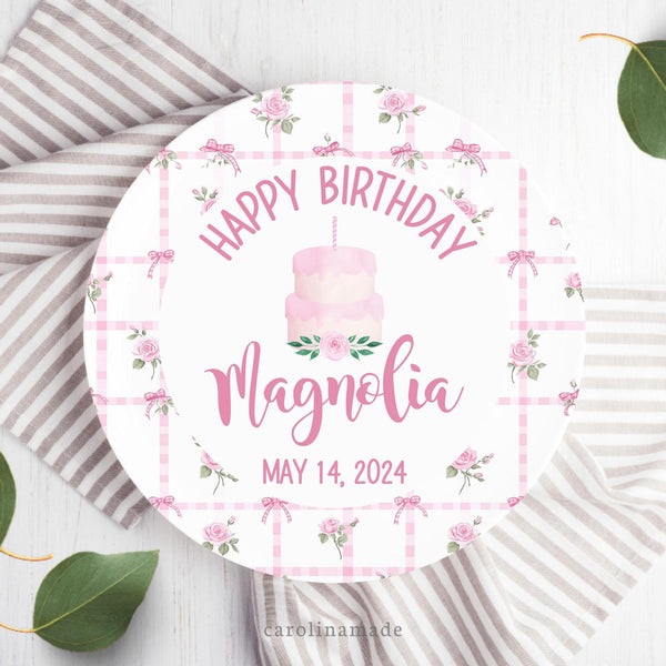 This white 10 inch plate features a pink rose and coquette bow background with a white center. It says Happy Birthday at the top, a cake in the middle and your childs name and date of birth at the bottom.