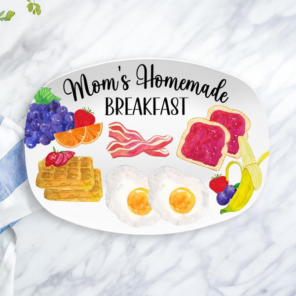 This white serving platter features the text Moms Homemade Breakfast and features different breakfast items on it. waffles, eggs, fruit, bacon and jelly toast. Personalize the text at the top.