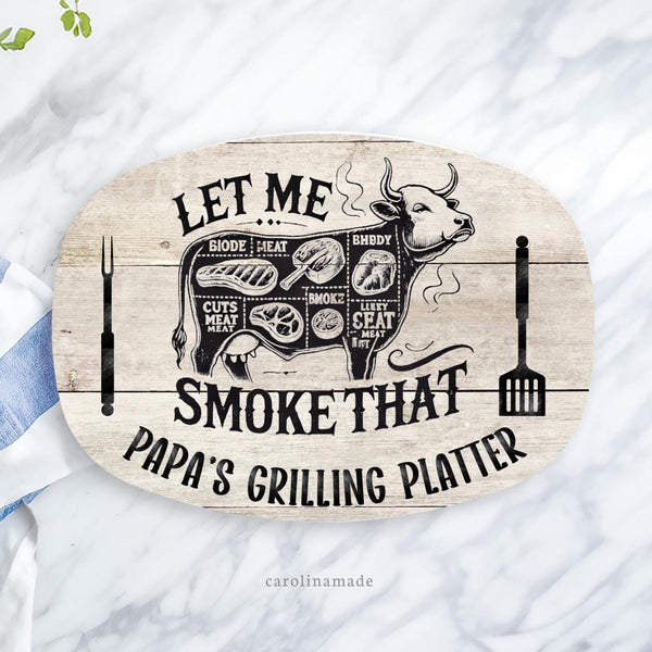 This grilling platter features a printed wood background with a cow in the center that shows the different cuts of meet. The platter says let me smoke that. And the bottom is personalized to say Papas grilling platter.