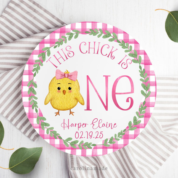 This ten inch birthday plate features a pink gingham scalloped ring with a greenery wreath and pink text that says This Chick is One and is personalized with your childs name and date of birth. The center is a baby chick with bow.