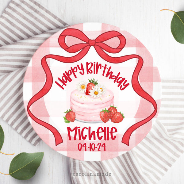 This personalized birthday plate features a red gingham background with a red grandmillenial bow around the plate. The center has a pink cake with strawberries and says Happy birthday with the persons name and date of birth.
