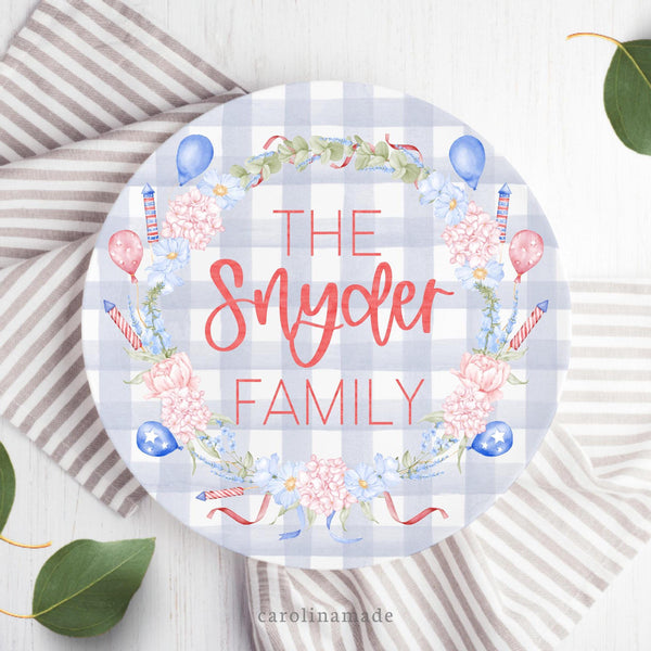 This fun patriotic plate features a blue gingham background with a red and blue flower wreath with greenery and American balloons and fireworks. The center is personalized with your family name.