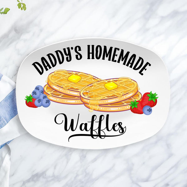This white serving platter features a personalized name at the top. This design shown says Daddys Homemade Waffles. The center has two stacks of waffles with butter and syrup and fresh strawberries and blueberries.
