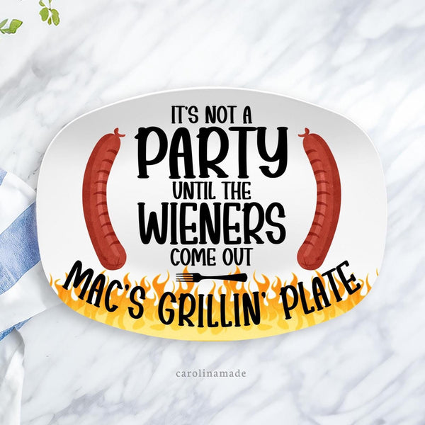 This white serving platter features a funny message in the center. Its not a party until the wieners come out. The bottom is personalized with a names grillin plate. The graphics feature flames at the bottom and two hot dogs around the text.