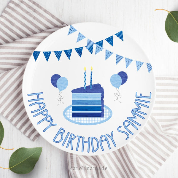 This 10 inch plate features white background and blue theme birthday design. A blue party banner at the top with a multi layer cake in the center in different shades of blue. The bottom says Happy birthday and is personalized with your childs name. The plate also features balloons in shades of blue.