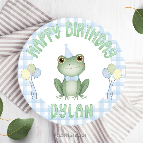 This 10 inch plate features a blue gingham background with a frog wearing a birthday hat and balloons in the center. The top says happy birthday and the bottom is personalized with your childs name.