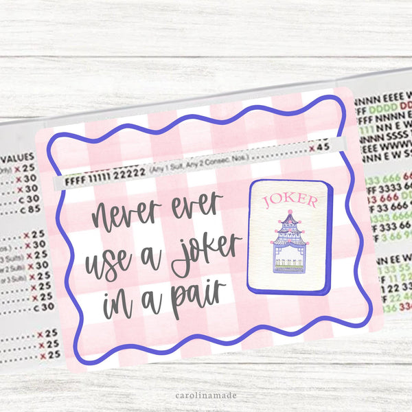 This acrylic mahjong line reader features a white and pink gingham background with a purple wavy border. Text is gray that says never ever use a joker in a pair with a joker mahjong tile. Matching zipper pouch available also.
