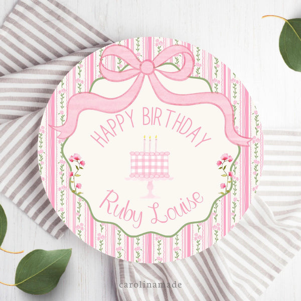 This 10" plastic plate features a pink stripes and floral outer background with a pink coquette bow at the top. The center says Happy Birthday and is personalized with your child's name. The center also has a cake with candles and flowers on each side.